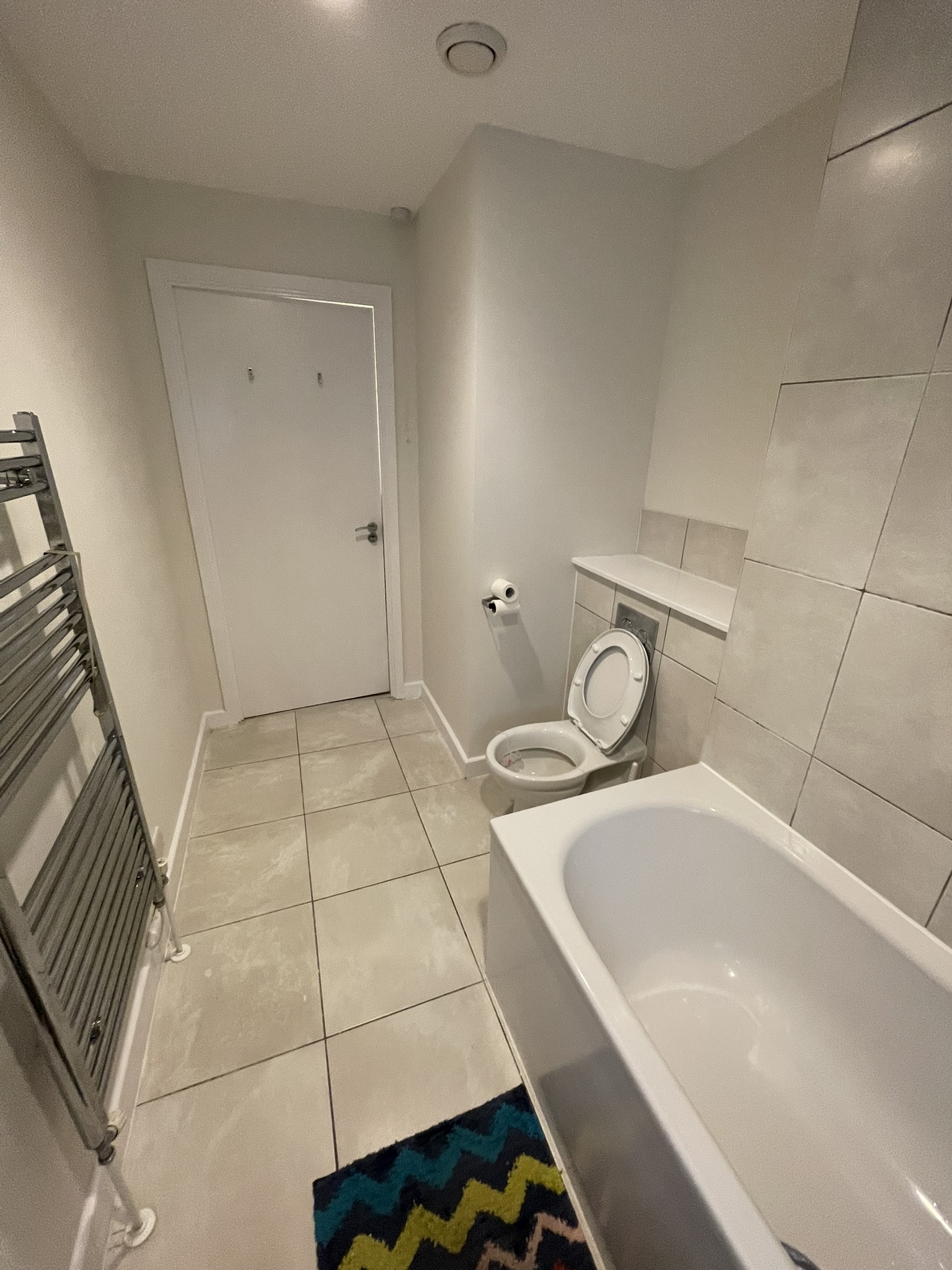 Family bathroom full view with WC, bath, chrome heated towel rail and large-format floor tiles by KDB Home Solutions