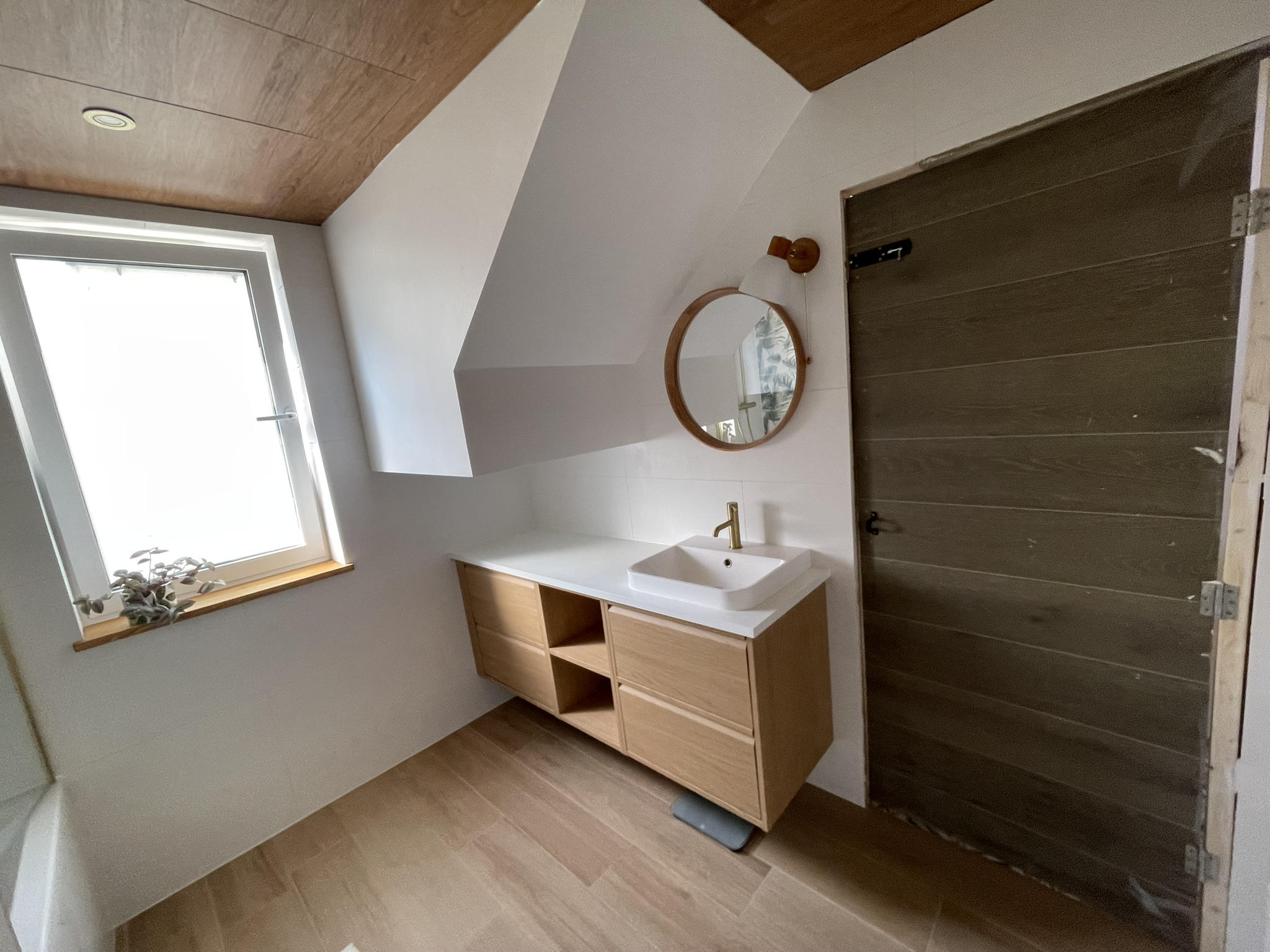 Loft bathroom vanity unit with oak finish, round mirror and Velux roof window by KDB Home Solutions