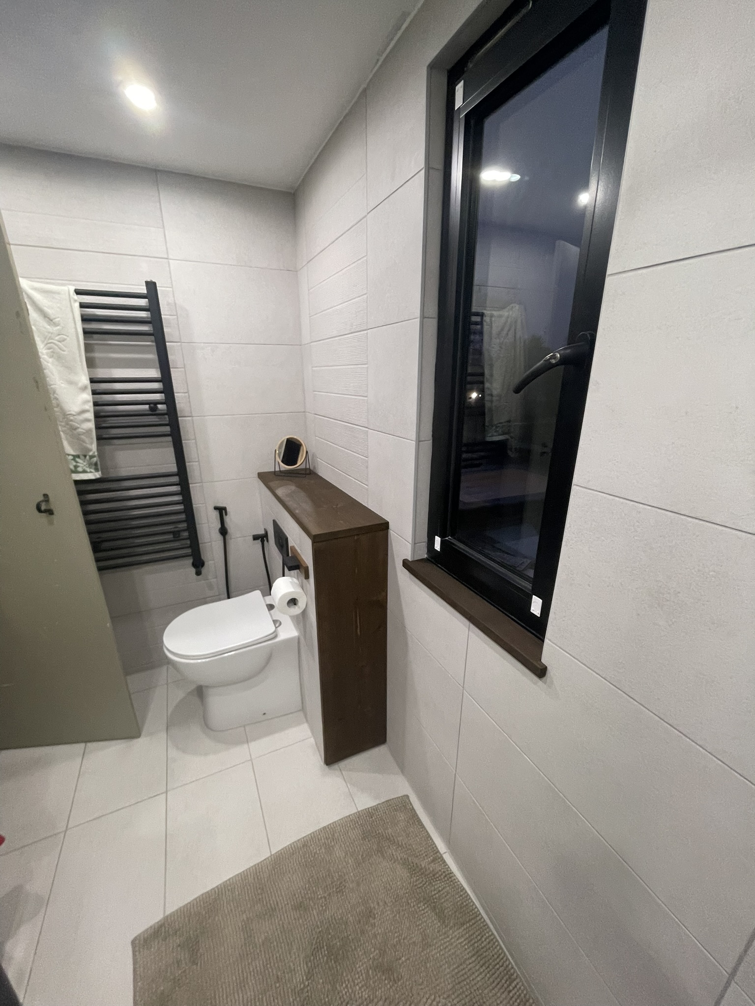 Modern bathroom with black heated towel rail, wall-hung WC and large format white tiles