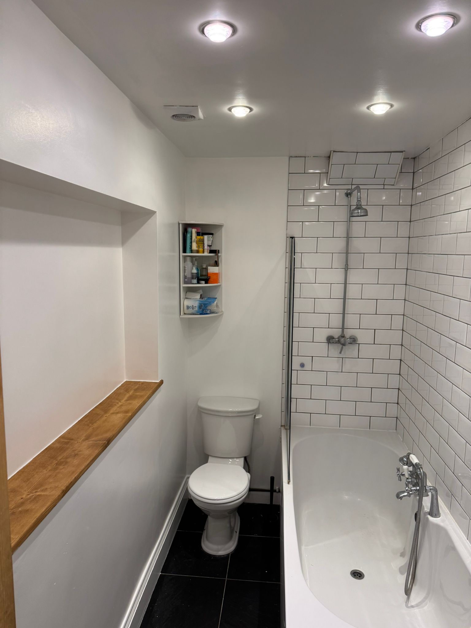 Bathroom renovation with white subway tiles, chrome shower rail, black floor tiles and bath by KDB Home Solutions