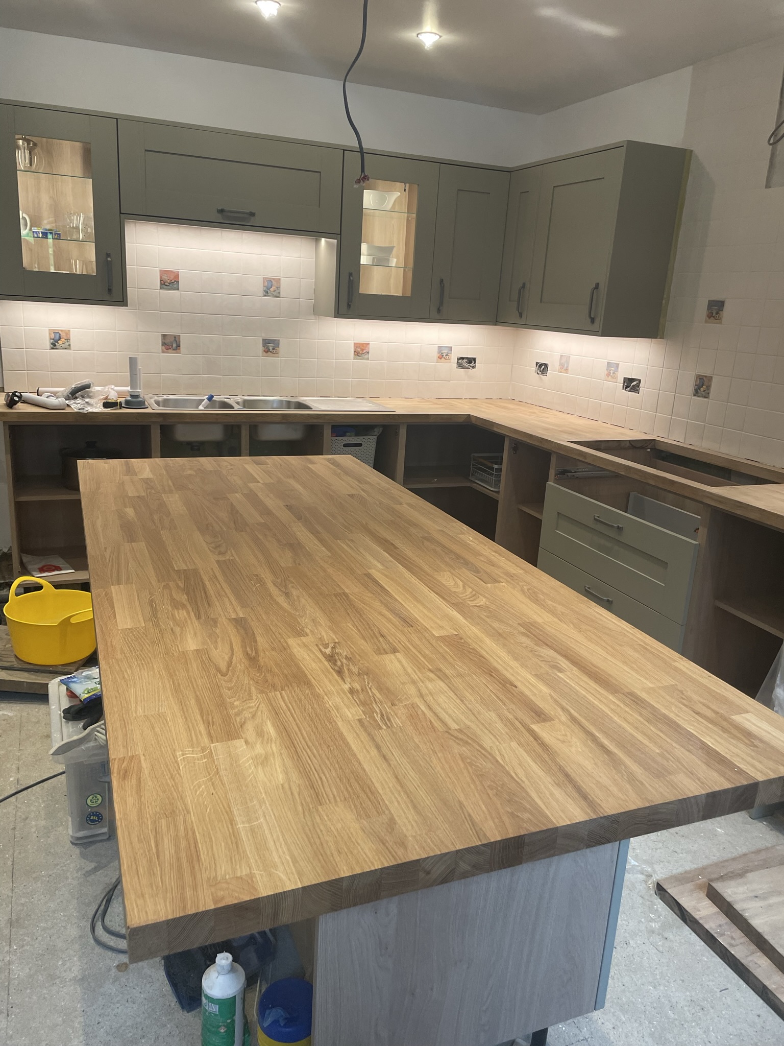 Sage green shaker kitchen with large solid oak island, oak worktops and glass-front display cabinets by KDB Home Solutions