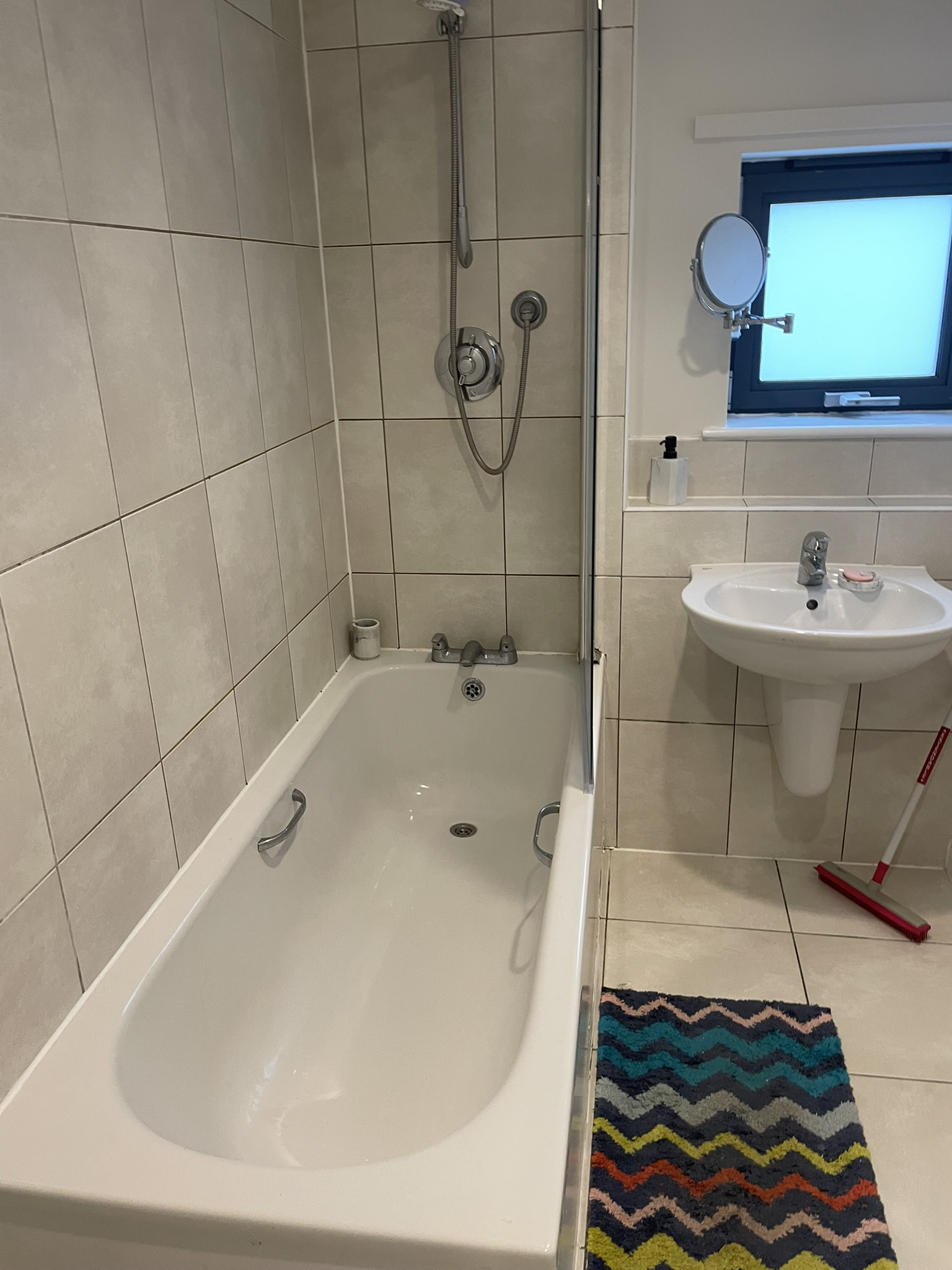 Family bathroom with large-format beige tiles, bath with shower over and pedestal basin by KDB Home Solutions