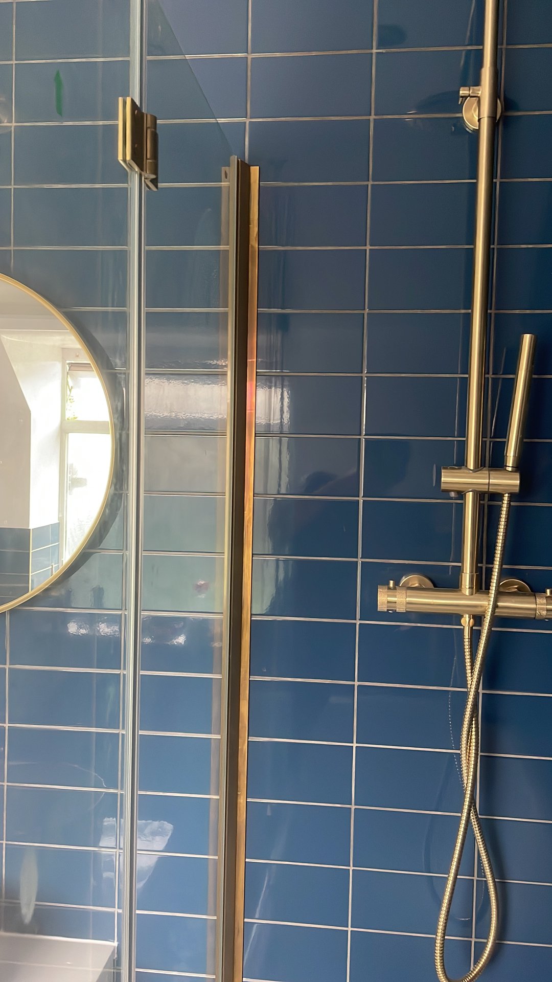 Shower room detail with bold blue wall tiles, brass shower rail and round mirror by KDB Home Solutions