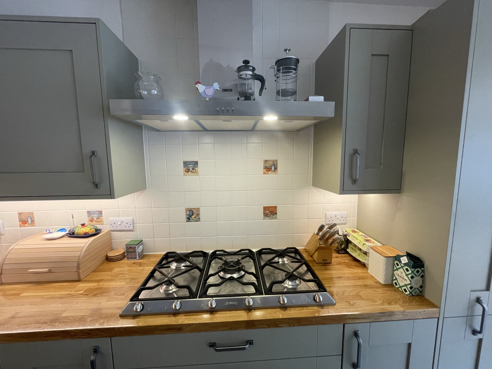 Grey-green shaker kitchen detail showing 5-burner gas hob, stainless steel extractor hood and oak worktop by KDB Home Solutions