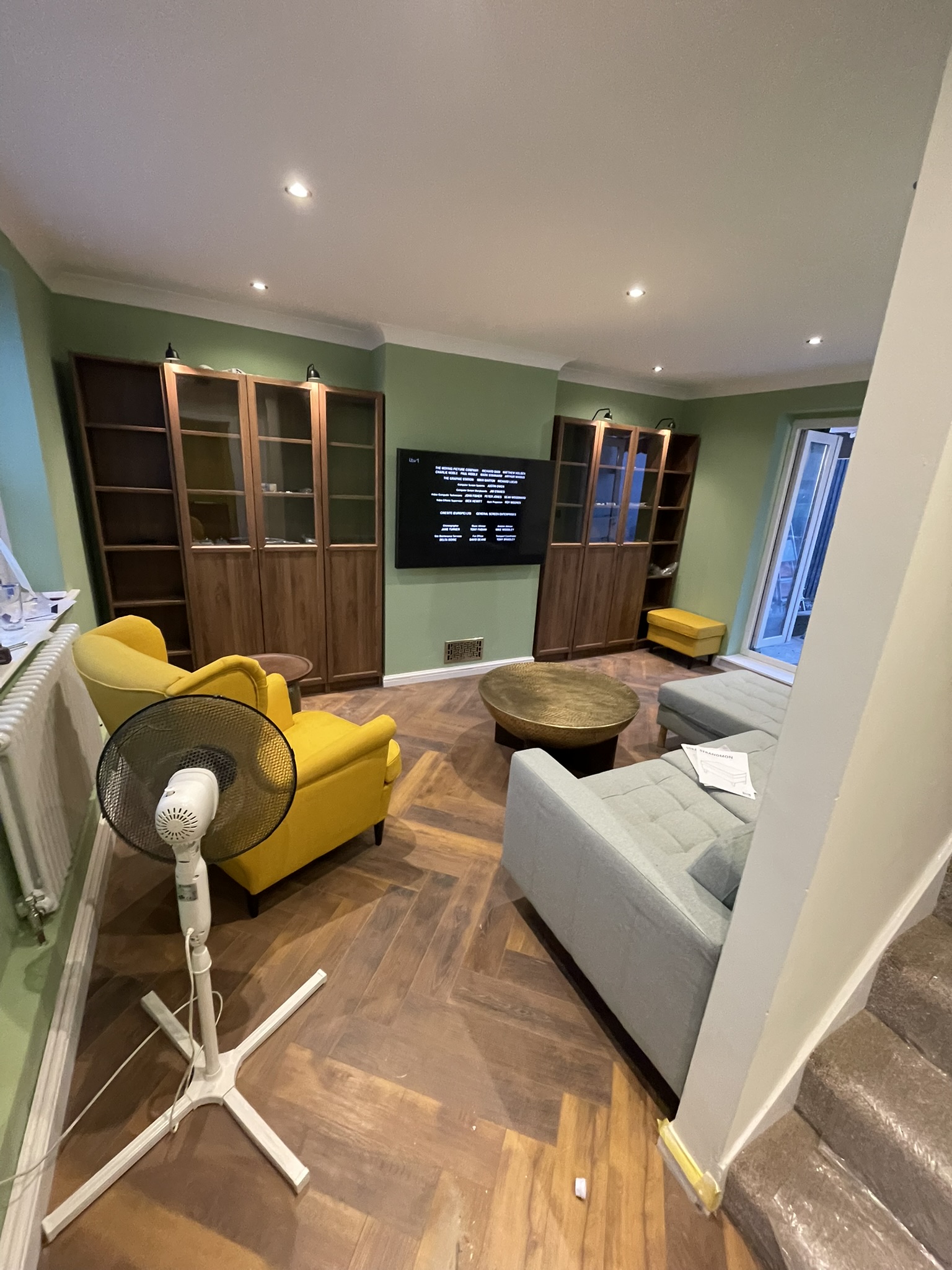 Refurbished living room with herringbone oak parquet flooring, sage green walls and fitted walnut display cabinets by KDB Home Solutions