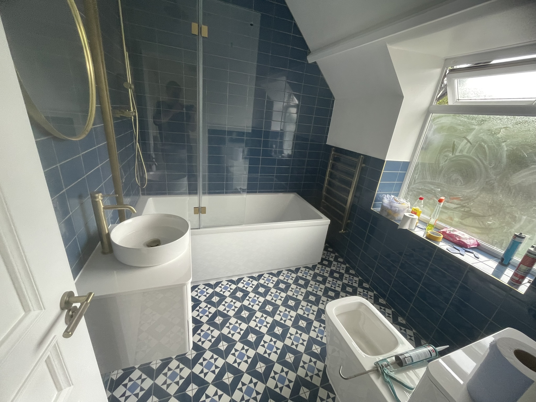 Loft bathroom with bold blue wall tiles, gold fixtures, ornate patterned floor tiles and bath by KDB Home Solutions