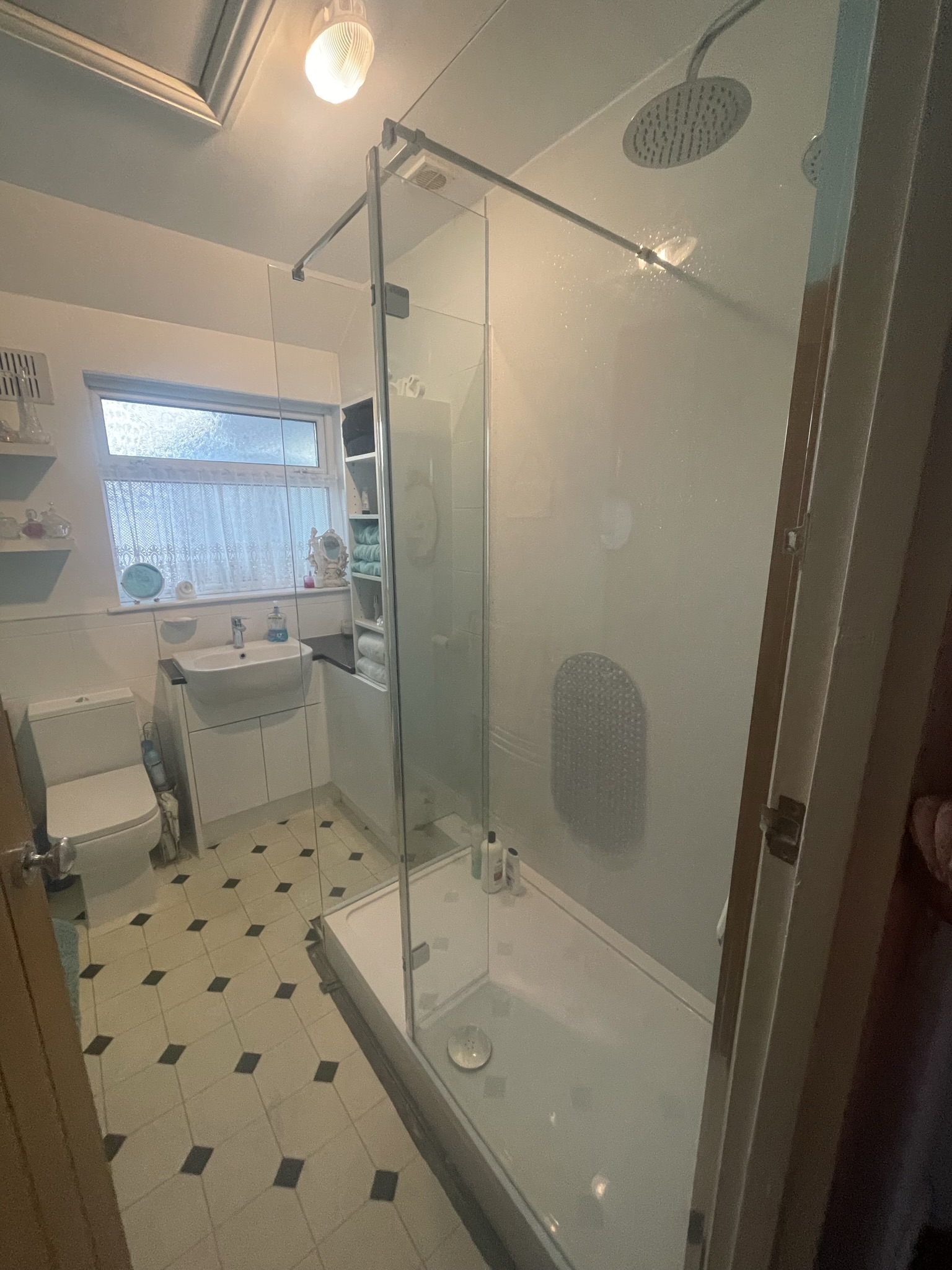 Compact shower room with chrome enclosure, rainfall head and classic black and white floor tiles by KDB Home Solutions