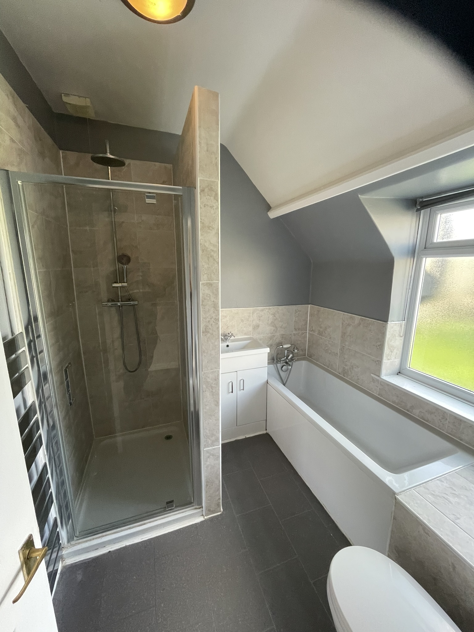 Loft conversion bathroom with separate shower enclosure, bath and beige stone tiles by KDB Home Solutions