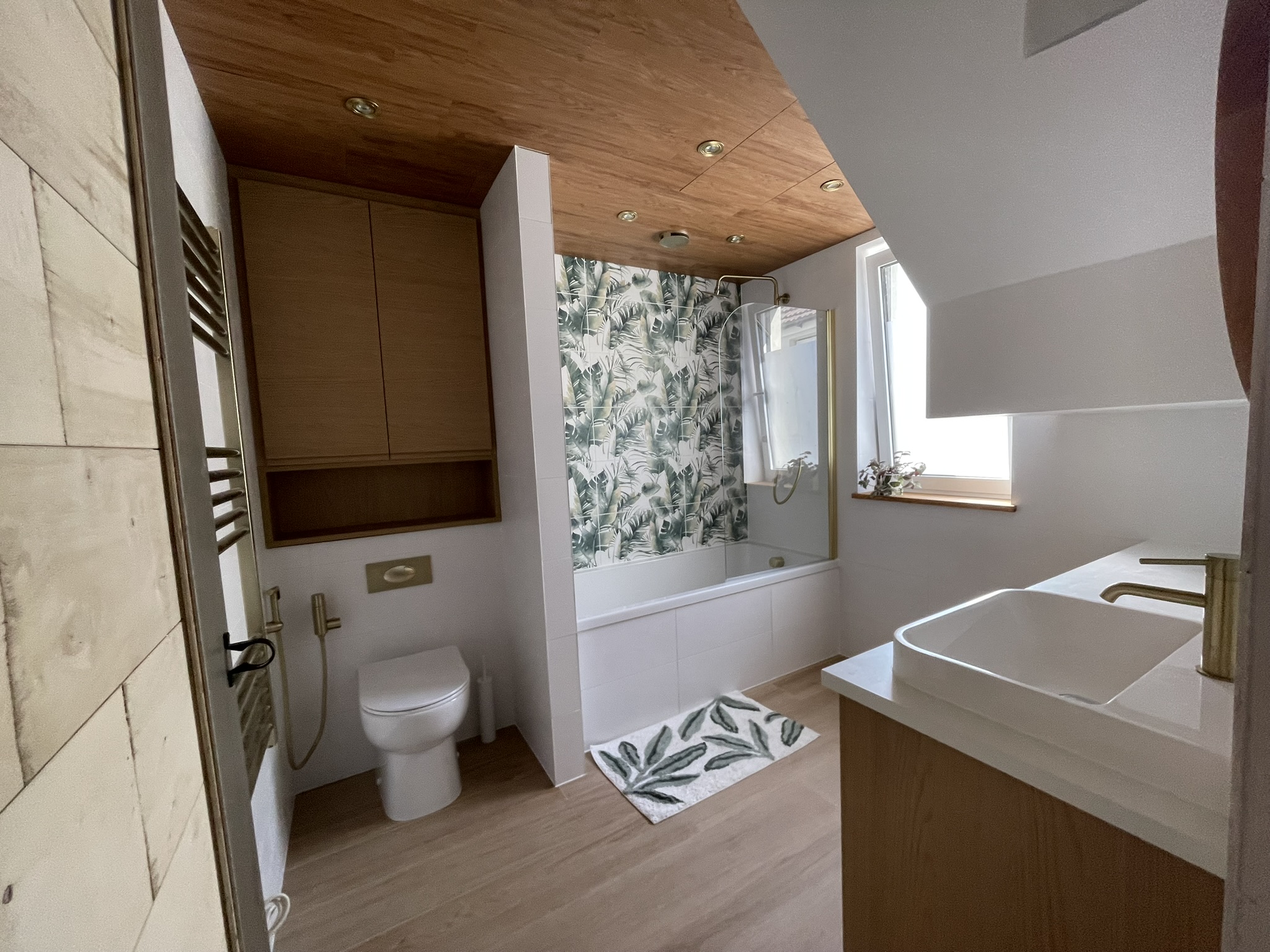 Full panoramic view of loft bathroom with WC, bath, botanical tiles and gold towel rail by KDB Home Solutions
