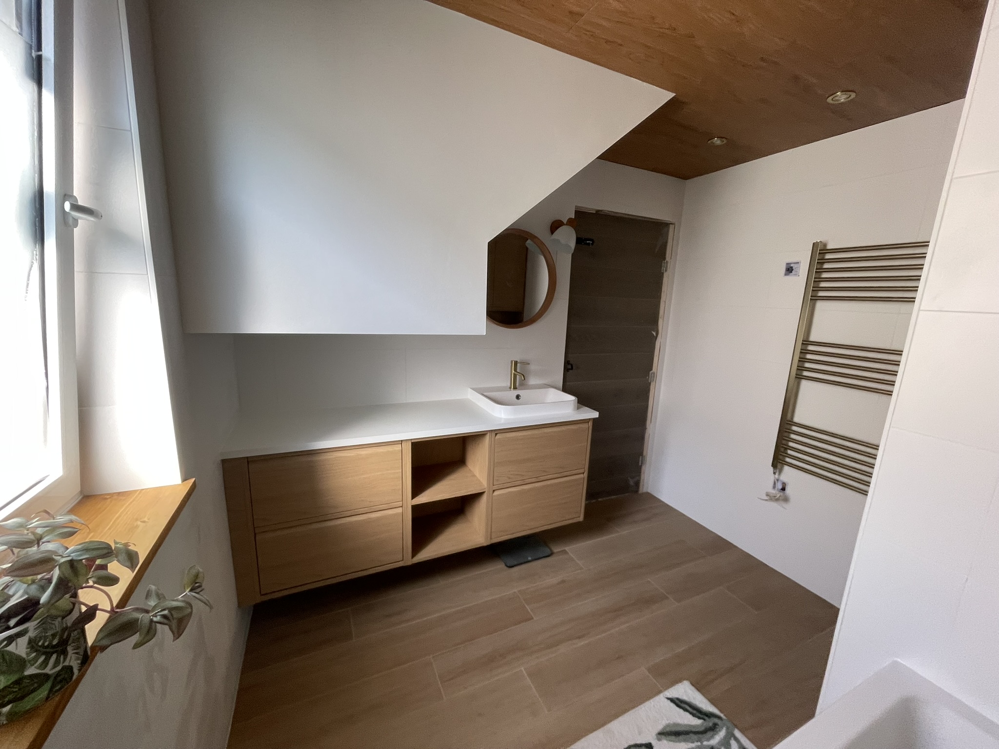 Loft bathroom with oak vanity, round mirror, gold heated towel rail and oak ceiling by KDB Home Solutions