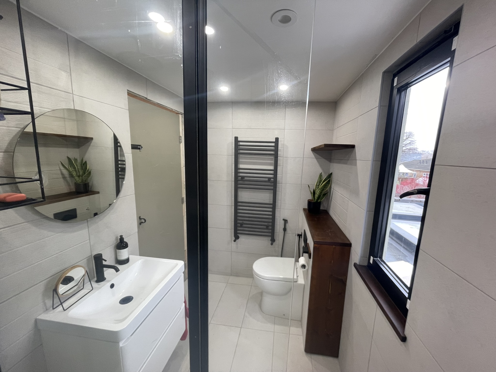 Modern bathroom with white large-format tiles, matte black heated towel rail, vanity unit and round mirror by KDB Home Solutions